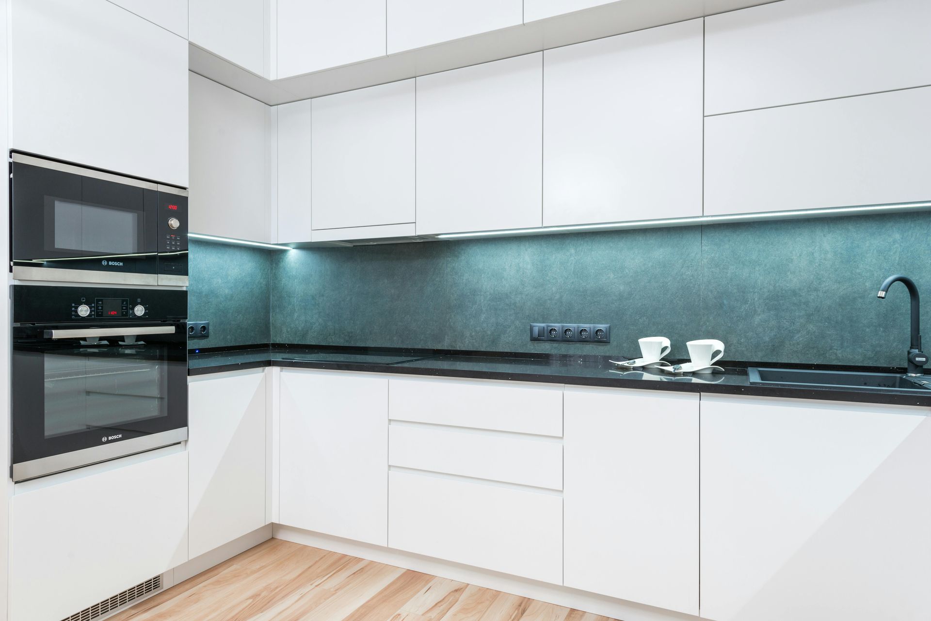 Modern white kitchen with black countertop, appliances, and backsplash.