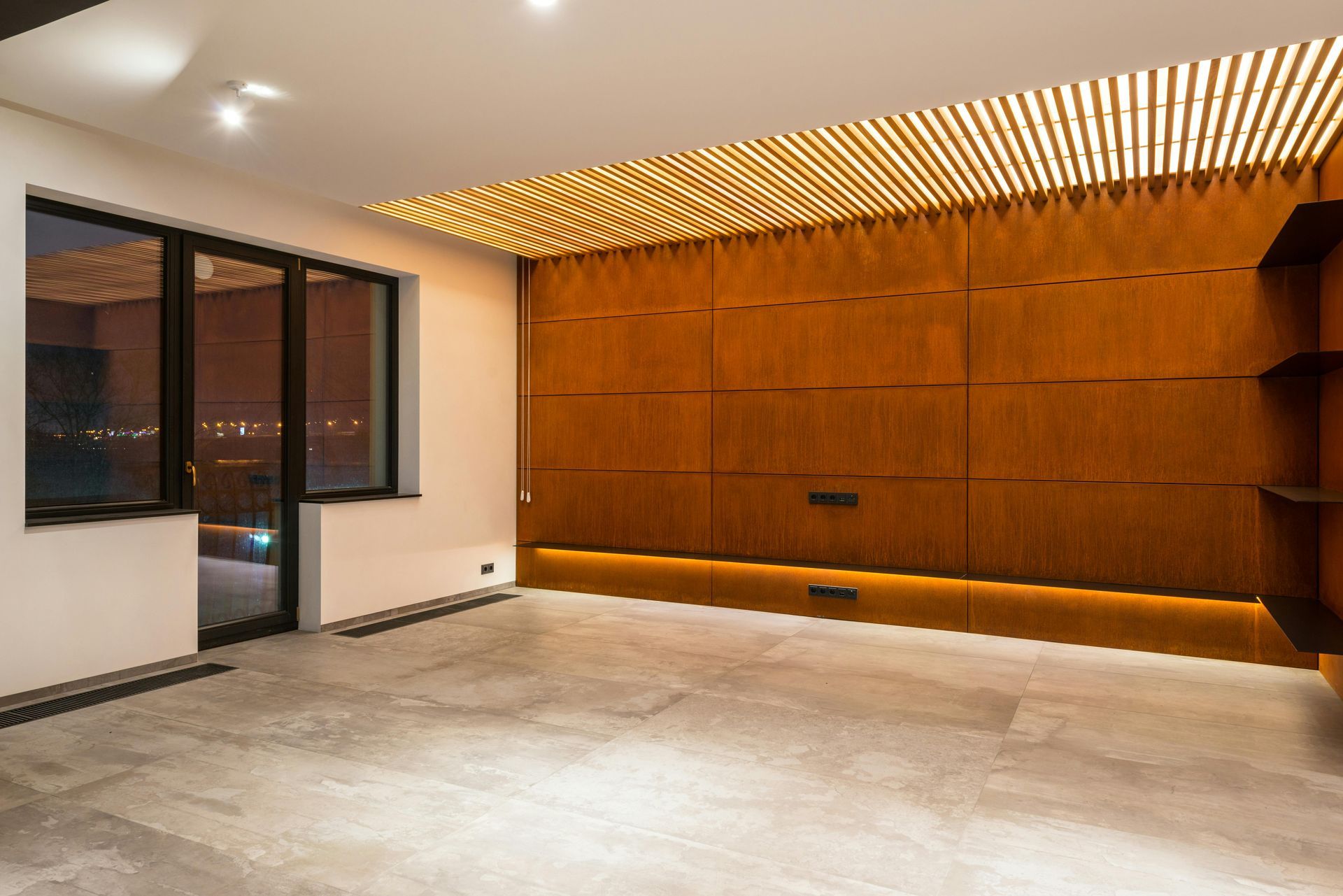 Empty modern room with wood paneling and shelving, large window, and light fixtures.
