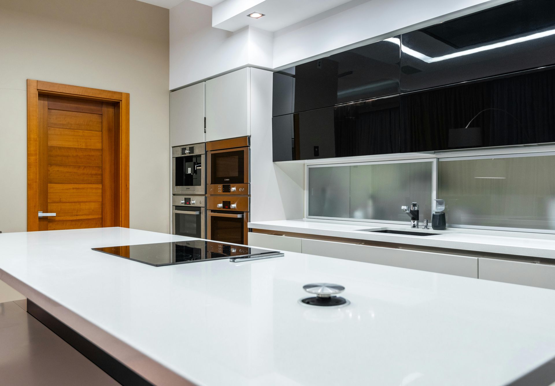 Modern kitchen with a white countertop island, black appliances, and wooden door.