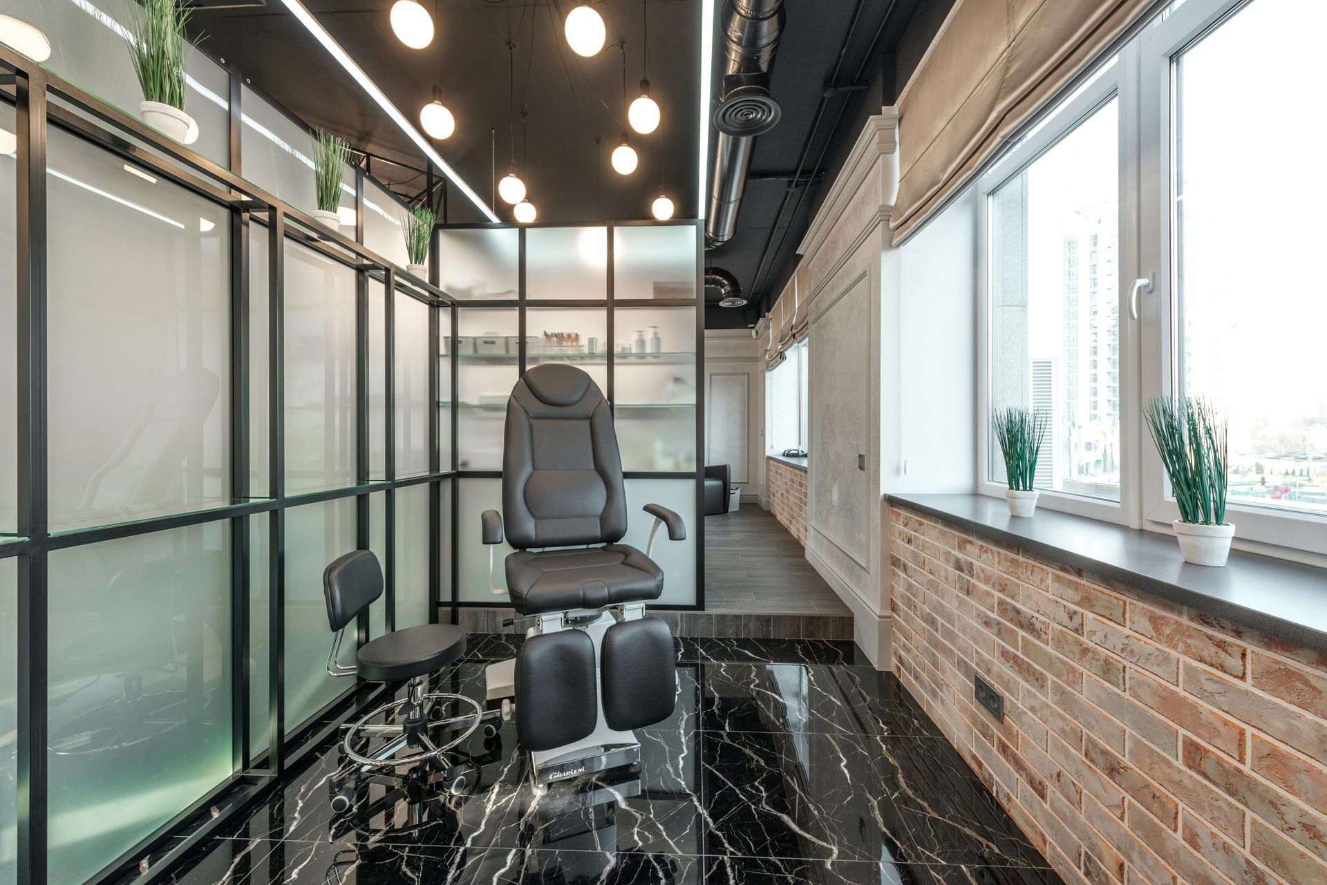 Treatment room with black chair, glass partitions, brick wall, and window.