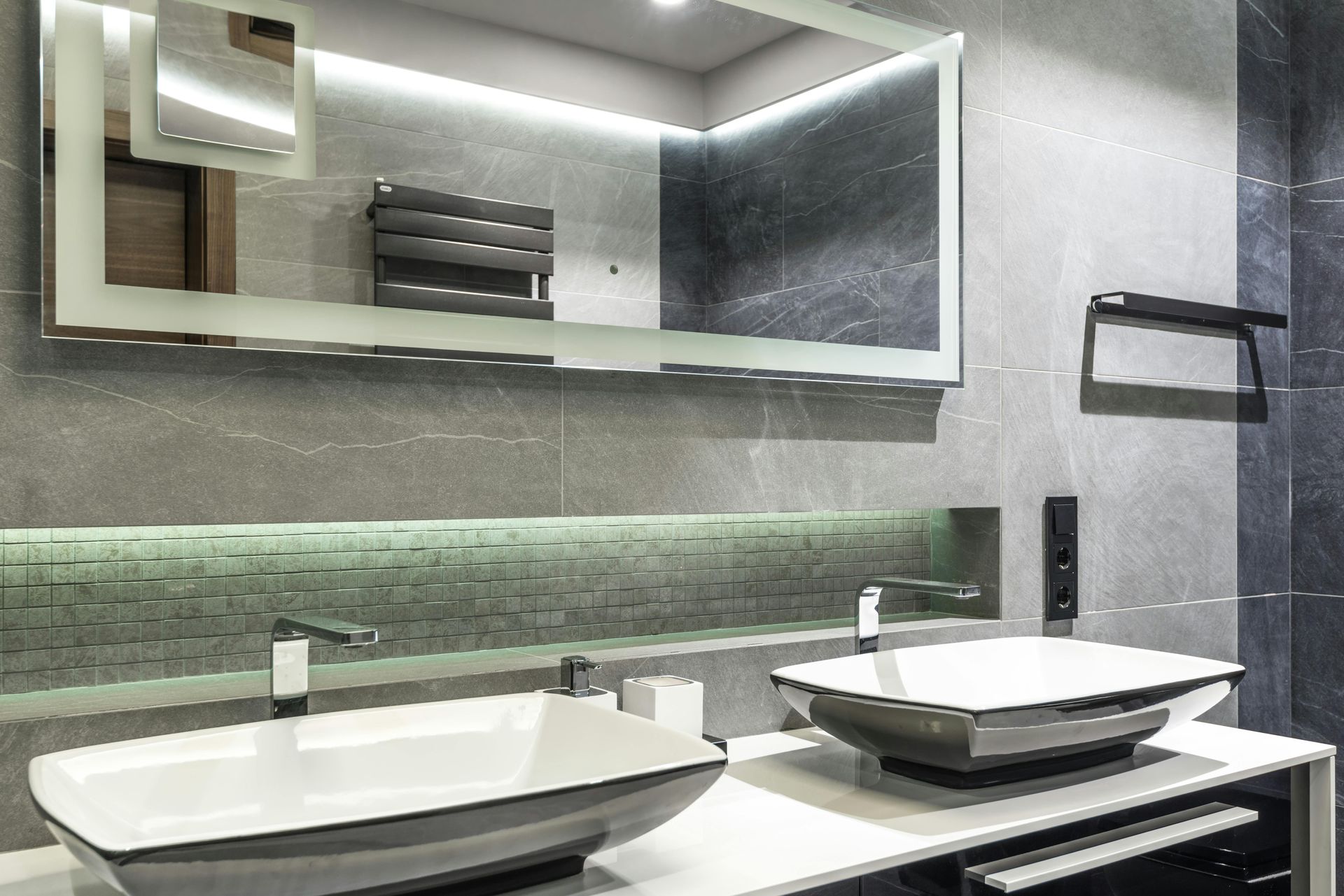 Modern bathroom with two sinks, large mirror, and gray tiled walls.