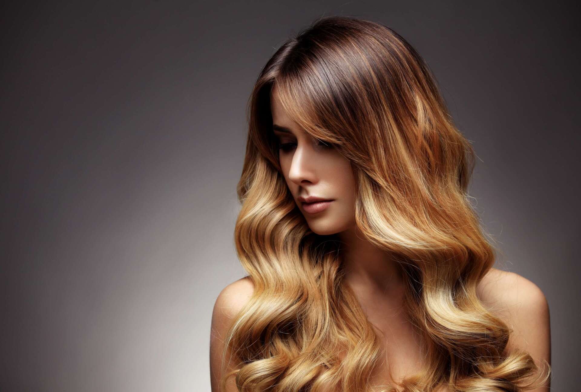 Donna con lunghi capelli castani ondulati su sfondo grigio scuro