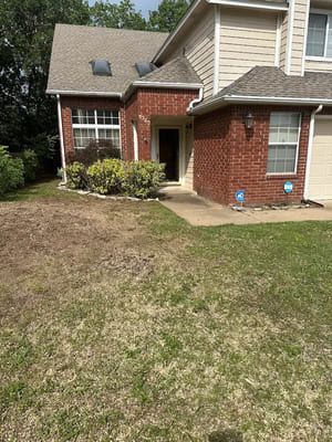A two-story house with red brick and beige siding, featuring a front entryway and a grassy lawn in the foreground.