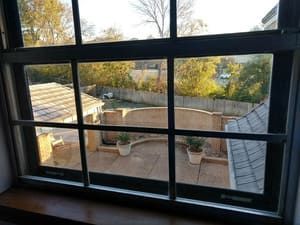 A view through a multi-paned window looking out onto a paved backyard patio with potted plants and a curved brick wall.