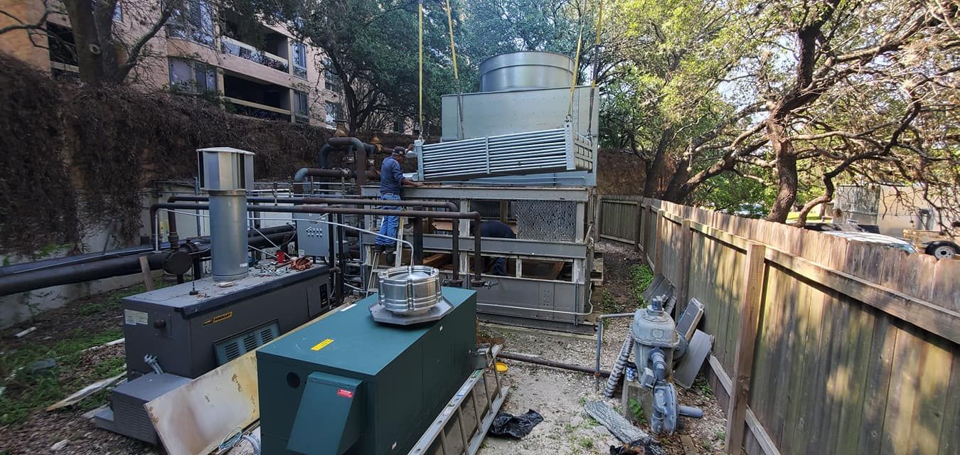 A man is working on a large machine in a backyard next to a fence.