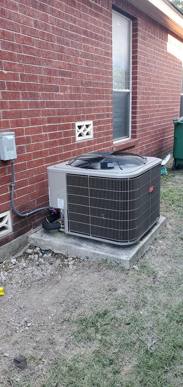 An air conditioner is sitting on the side of a brick house.
