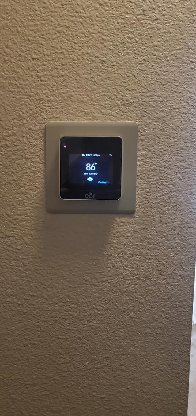 A thermostat is mounted on a wall next to a window.