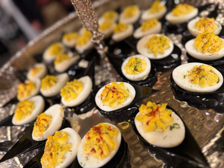 A tray of stuffed eggs on black spoons on a table.