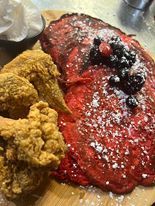 Fried chicken next to a large red pancake topped with berries and powdered sugar.
