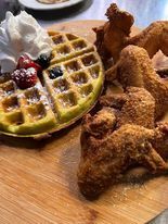 Chicken and waffles with whipped cream and berries on a wooden serving board. The fried chicken is golden brown.