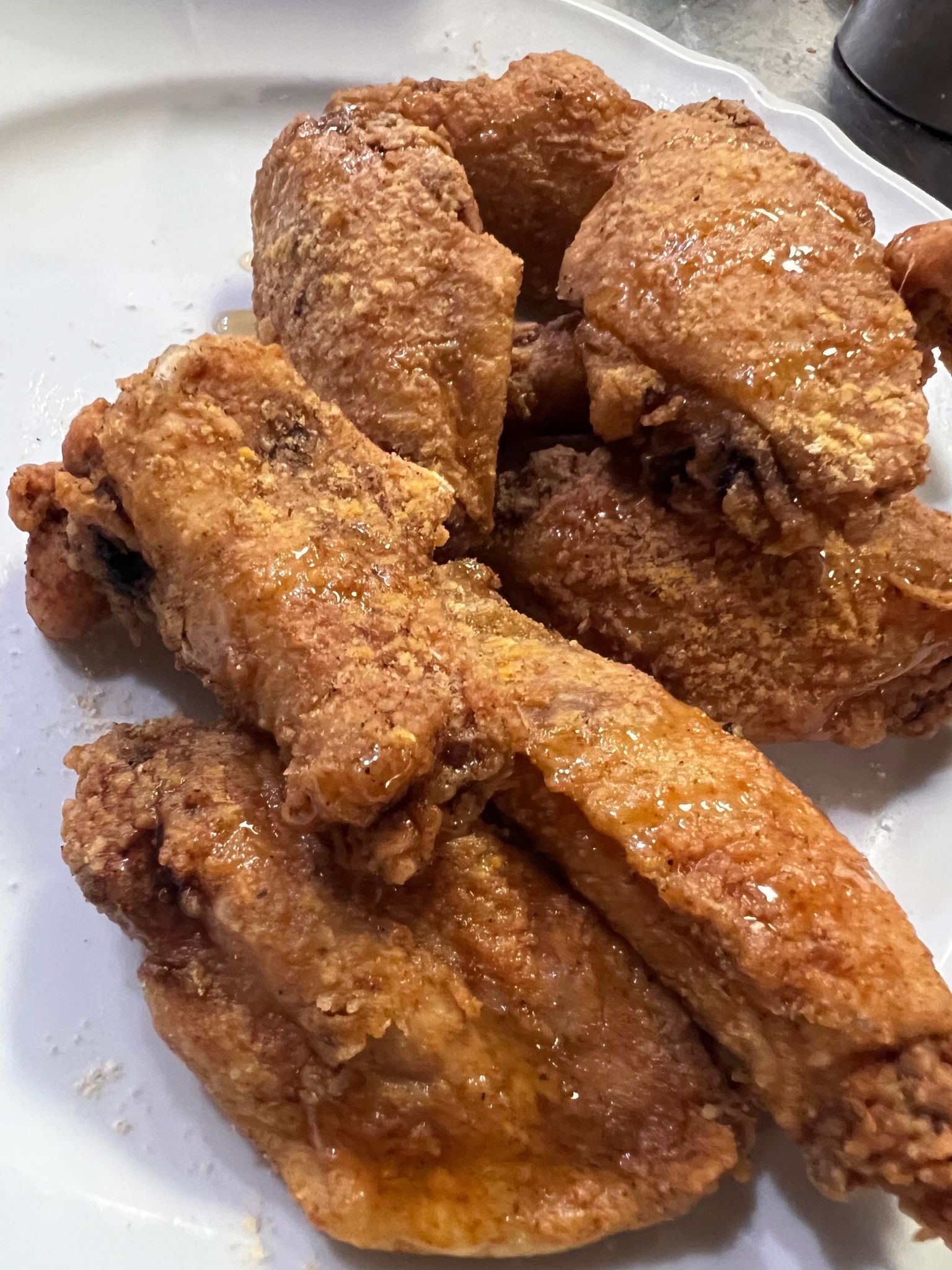 Close-up of golden-brown fried chicken wings on a white plate, glistening with sauce and seasoning.