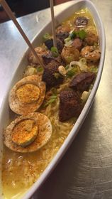 Ramen in a white oval dish; includes noodles, seasoned eggs, shrimp, meat, and chopsticks.