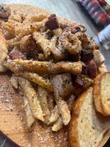 Close-up of a wooden board with a hearty meal: pasta, seasoned fries, sausage, and garlic bread.