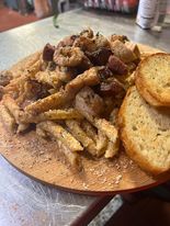 Fries topped with meat and a side of toasted bread served on a wooden plate.