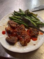 Plate of food: cooked meat in sauce, green beans, and a fork on a white plate.