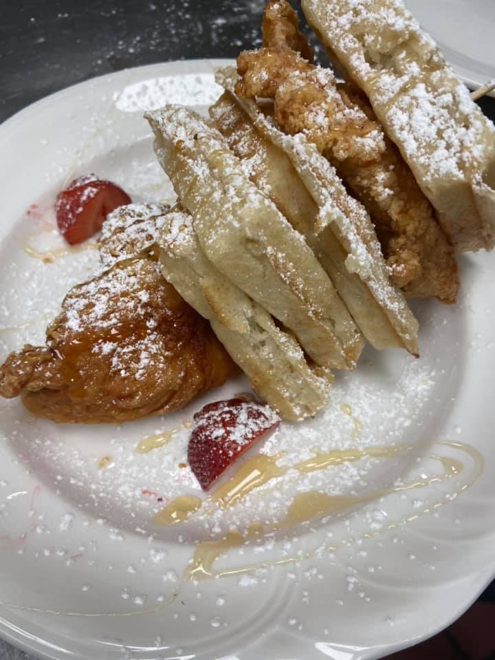 Plate of fried pastries dusted with powdered sugar, drizzled with syrup, and garnished with strawberries.