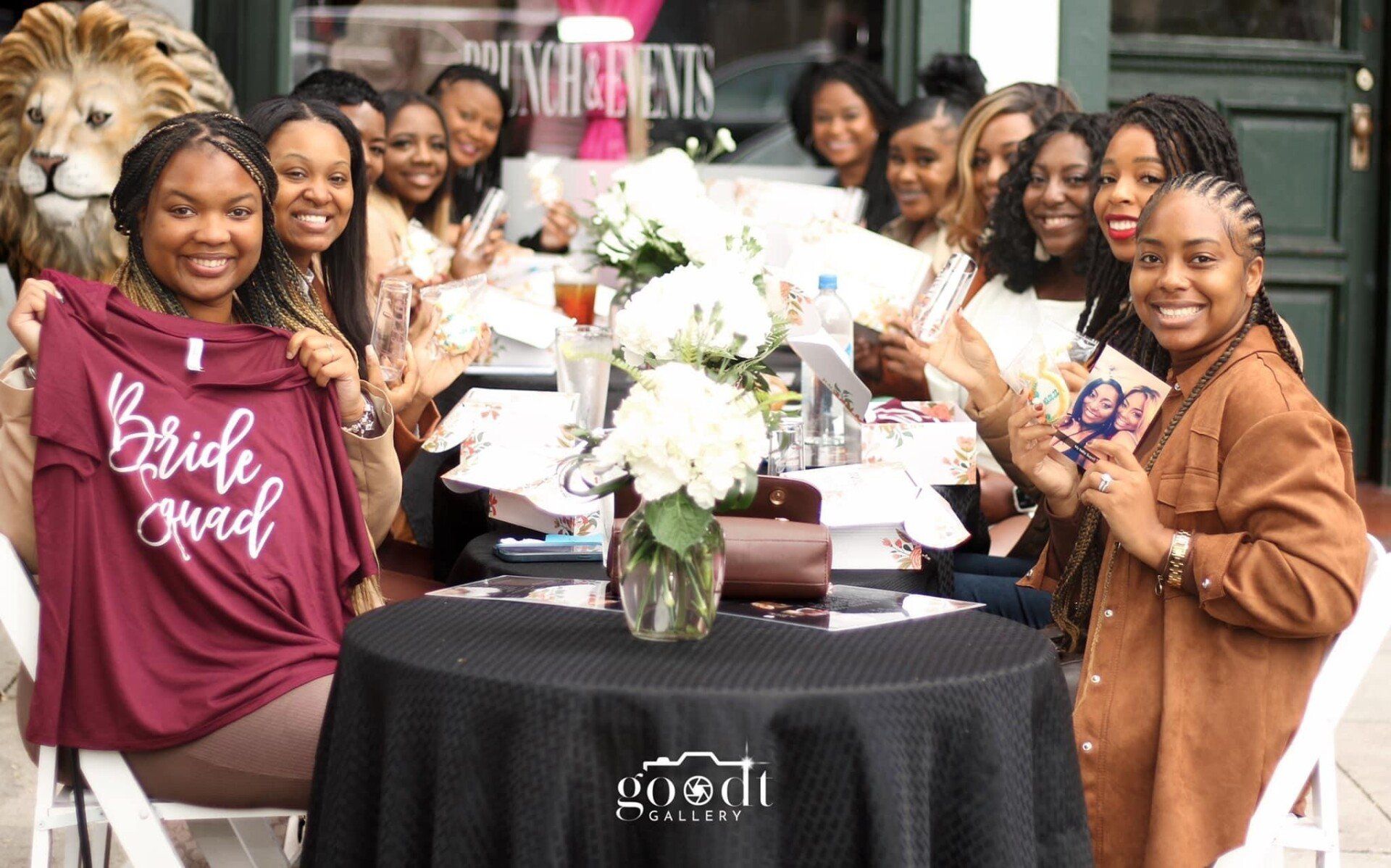Group of Black women at a table, celebrating a bride. One holds a