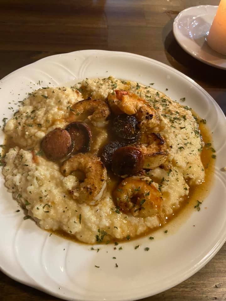 Shrimp and grits with sausage on a white plate, garnished with herbs. Warm lighting, close-up view.