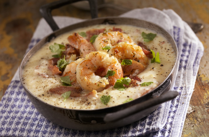 Shrimp and grits in a dark bowl, garnished with parsley and bacon, on a checkered cloth. Shrimp and grits in a dark bowl, garnished with parsley and bacon, on a checkered cloth.