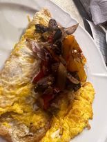 Omelette filled with a topping of sauteed vegetables, including mushrooms and peppers, on a white plate.