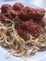 Spaghetti with meatballs in red sauce, sprinkled with herbs, served on a white plate.
