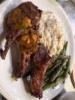 Plate with lamb chops, mashed potatoes, and green beans. The chops are browned, potatoes are speckled, and beans are a vibrant green.