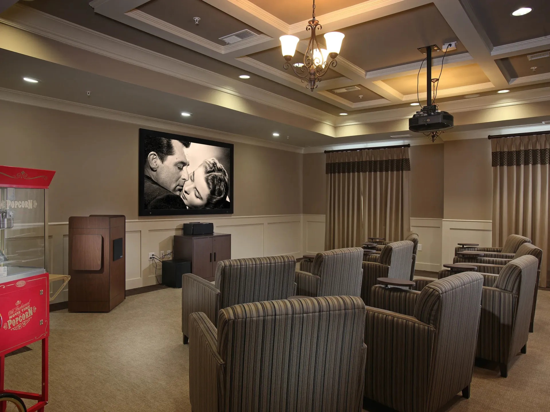 Community theater/lounge with projector screen, popcorn machine, and rows of seating.