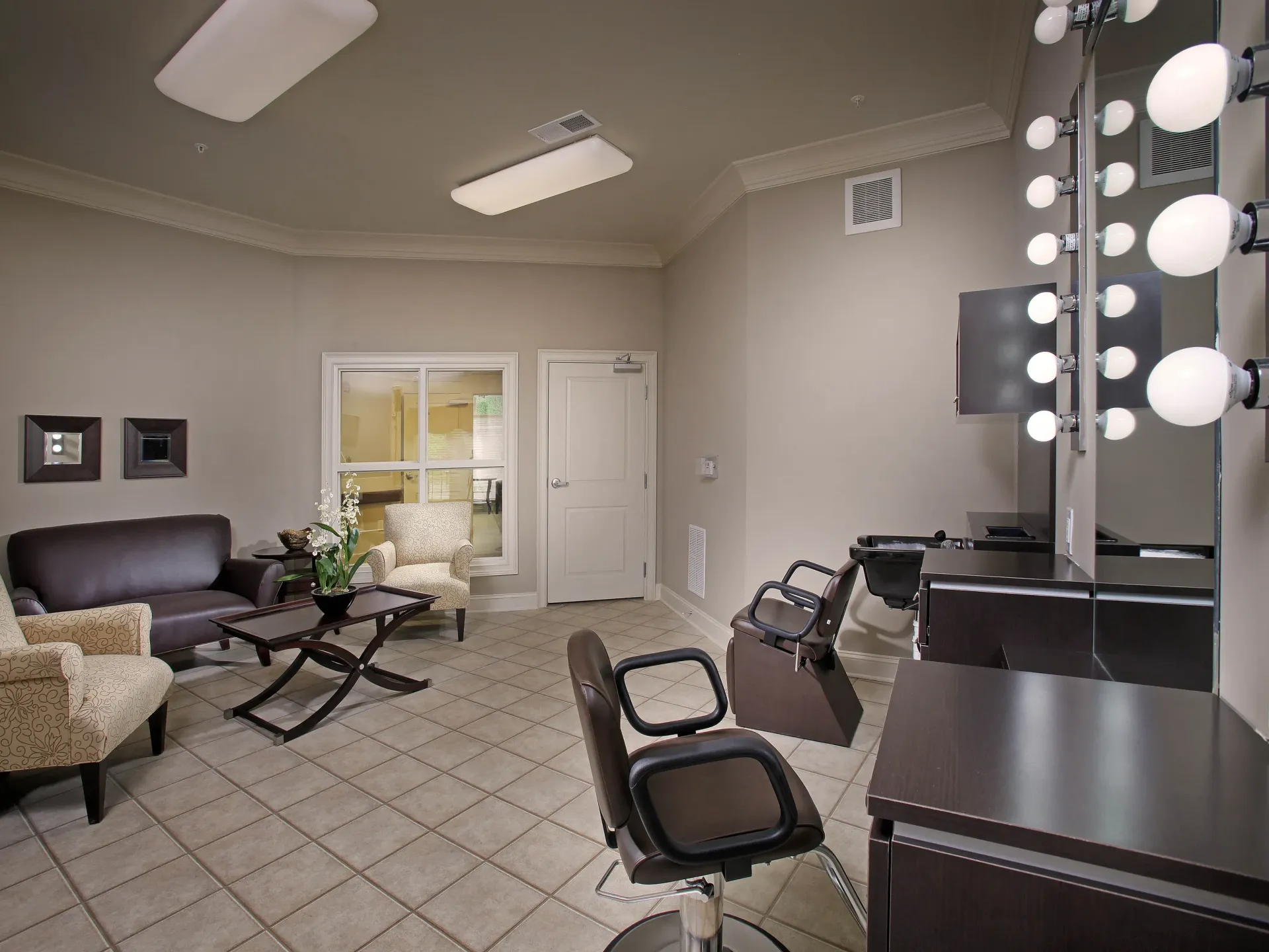 Salon-style makeup vanity with illuminated bulbs around mirrors and seating.