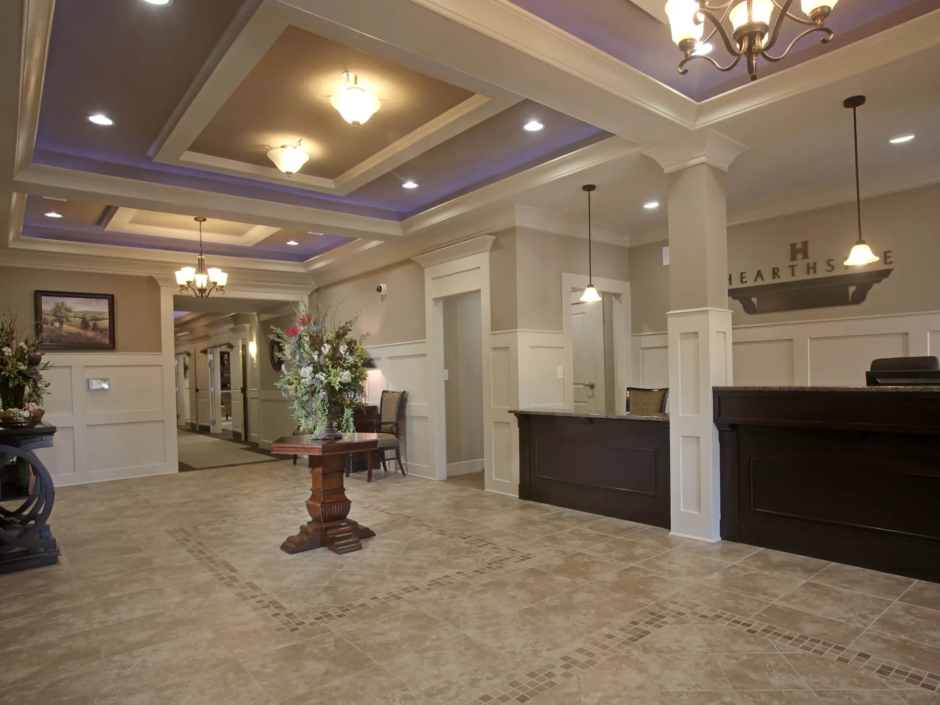 Bright apartment community lobby with chandeliers, reception desk, and tile floor.