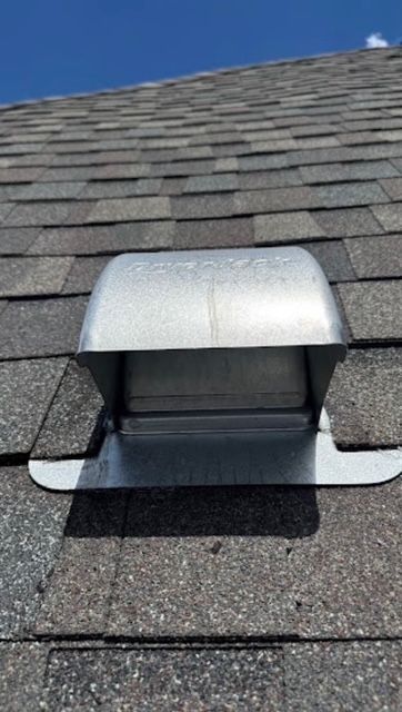 Silver metal roof vent on gray asphalt shingles against a blue sky.