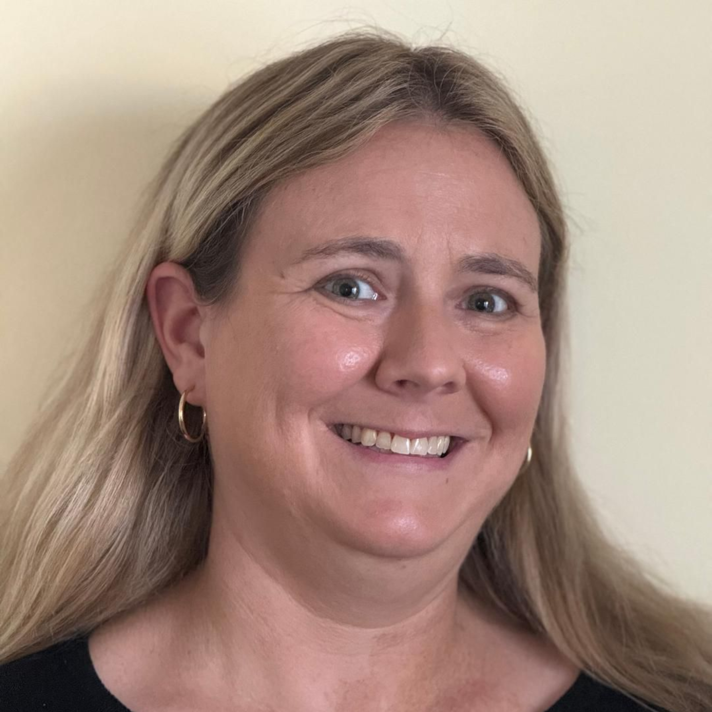 Woman with blond hair smiles at the camera, wearing a black top.