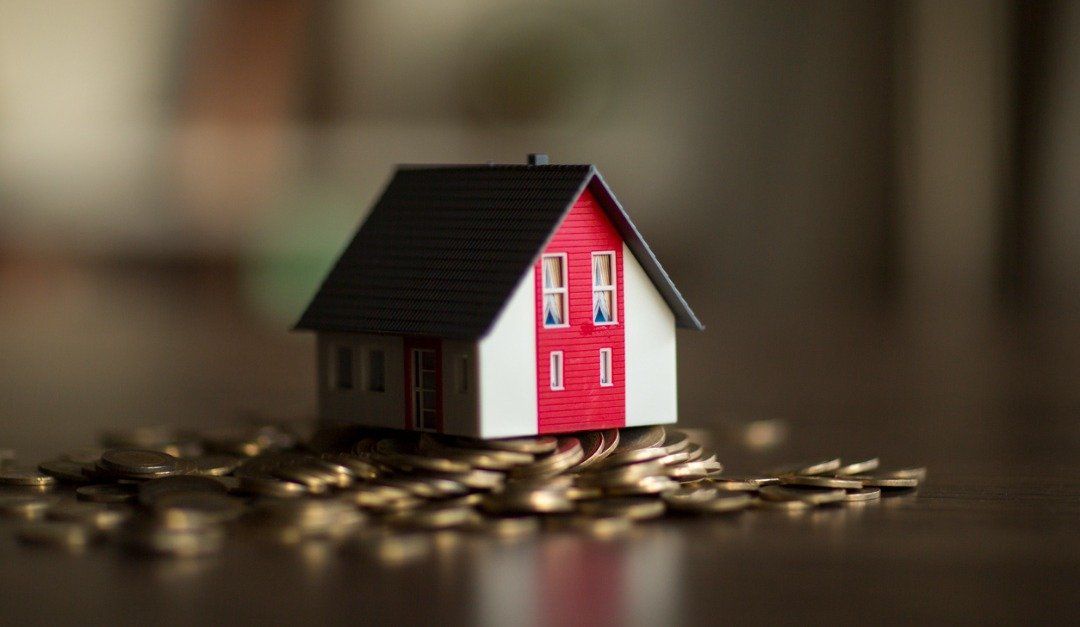 Toy house with red accents sits atop a pile of gold coins.
