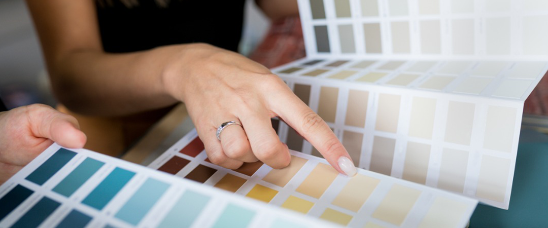 Person's hand pointing at paint swatches, selecting colors for a design project.