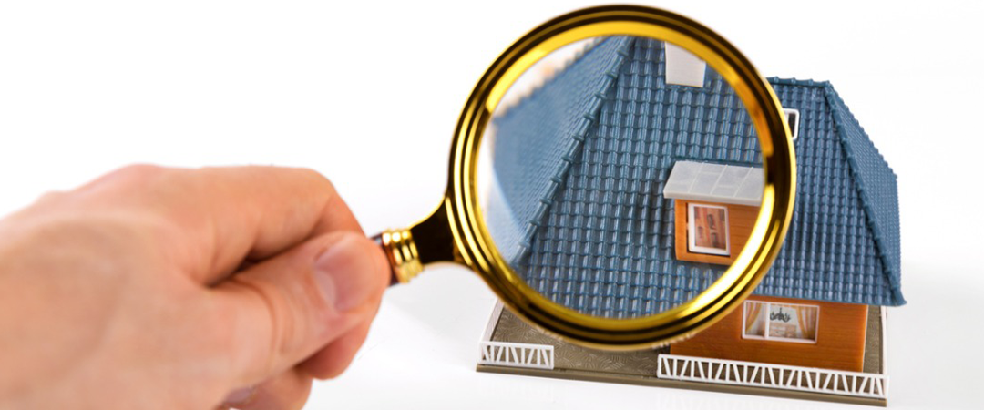 Hand holding magnifying glass over miniature house.