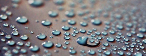 Close-up of water droplets on a surface, reflecting light. The drops vary in size.