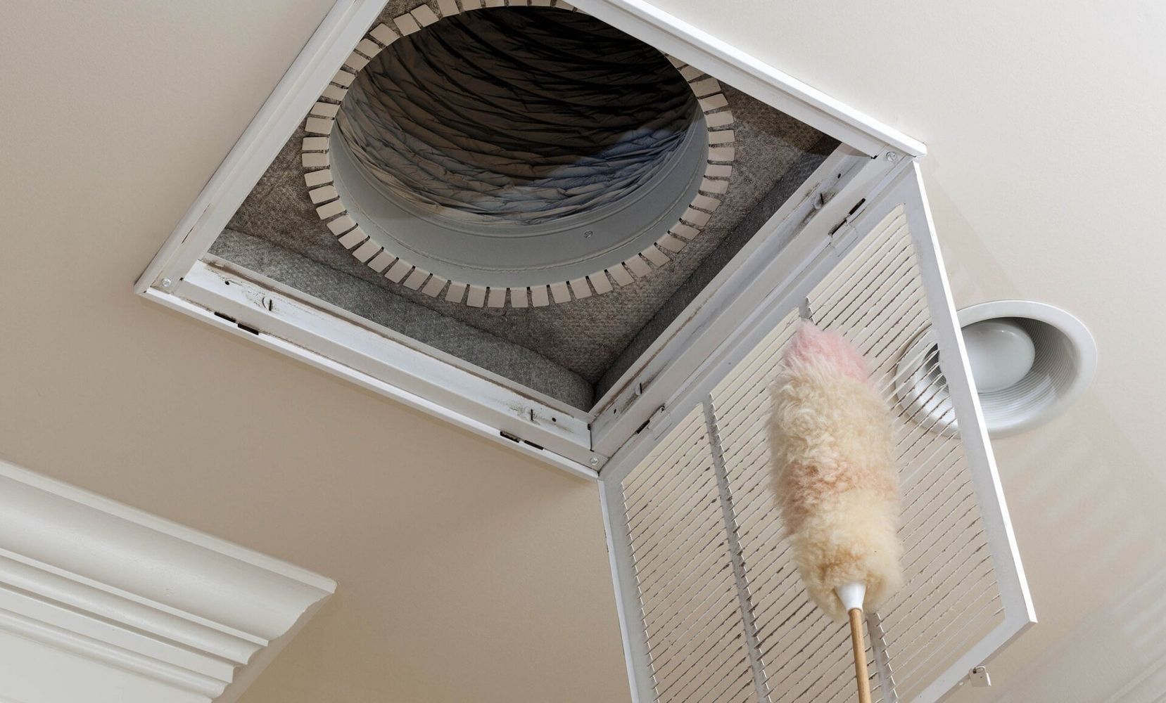 A person is cleaning a ceiling vent with a duster.