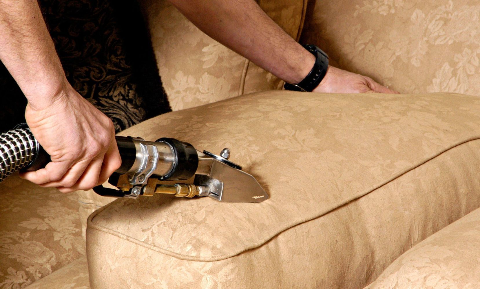 A person is cleaning a couch with a vacuum cleaner.