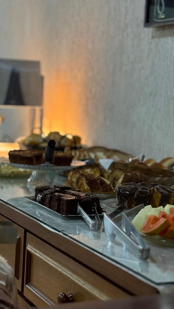 Buffet de sobremesas com bolos e doces em uma mesa em uma sala com iluminação suave.