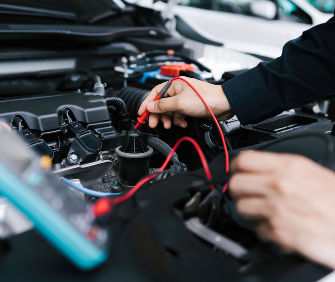 A person is working on a car engine with a multimeter.  | Greatway Tire and Auto Center