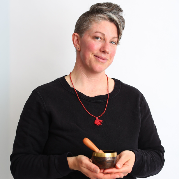 Person holding a singing bowl and mallet, wearing a black shirt and red necklace against a white background
