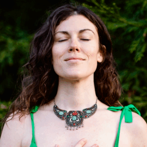Woman with closed eyes wearing a green dress and ornate necklace outdoors