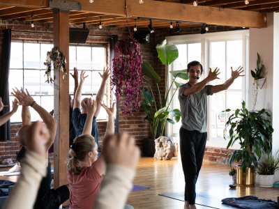 Instructor leading a yoga class in a bright studio with participants stretching on mats