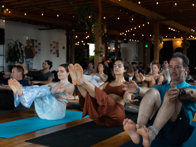 Group doing yoga poses on mats in a warmly lit studio with string lights and wooden beams