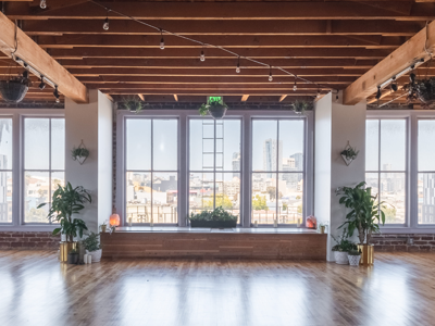 Bright, empty loft with large windows, exposed wooden beams, polished floor, and city skyline view