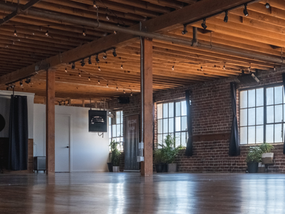 Empty industrial loft interior with exposed brick, wood ceiling beams, large windows, and polished floors