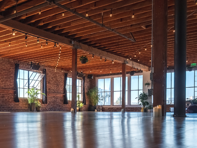 Empty loft with exposed brick, wooden beams, large windows, and polished concrete floor.