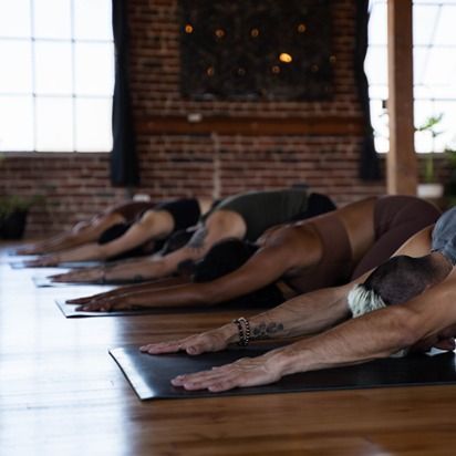 People doing yoga stretches on mats in a brick-walled studio