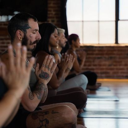 People seated in a yoga class, meditating on mats in a sunlit studio
