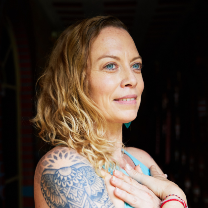 Woman with wavy hair and tattooed shoulder, smiling in profile against a dark background