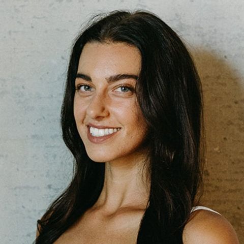 Smiling woman with long dark hair against a light gray wall